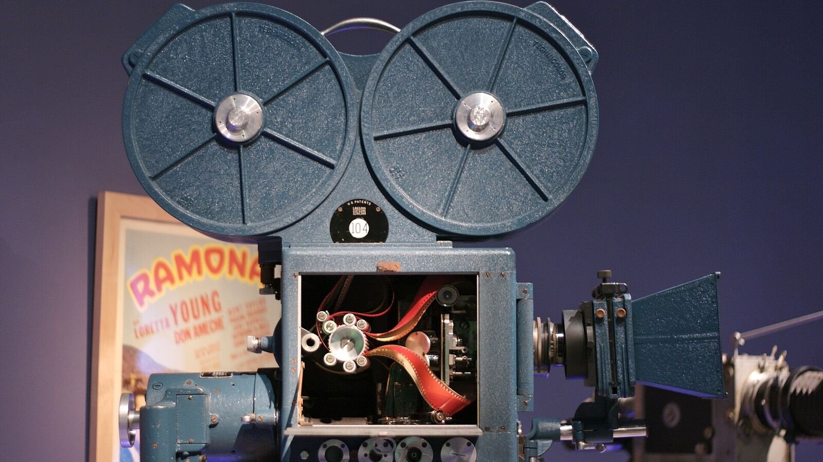 A large boxy 1930s three-strip Technicolor motion picture camera in a museum display, with its magazines on top and a lens protruding from a padded housing.