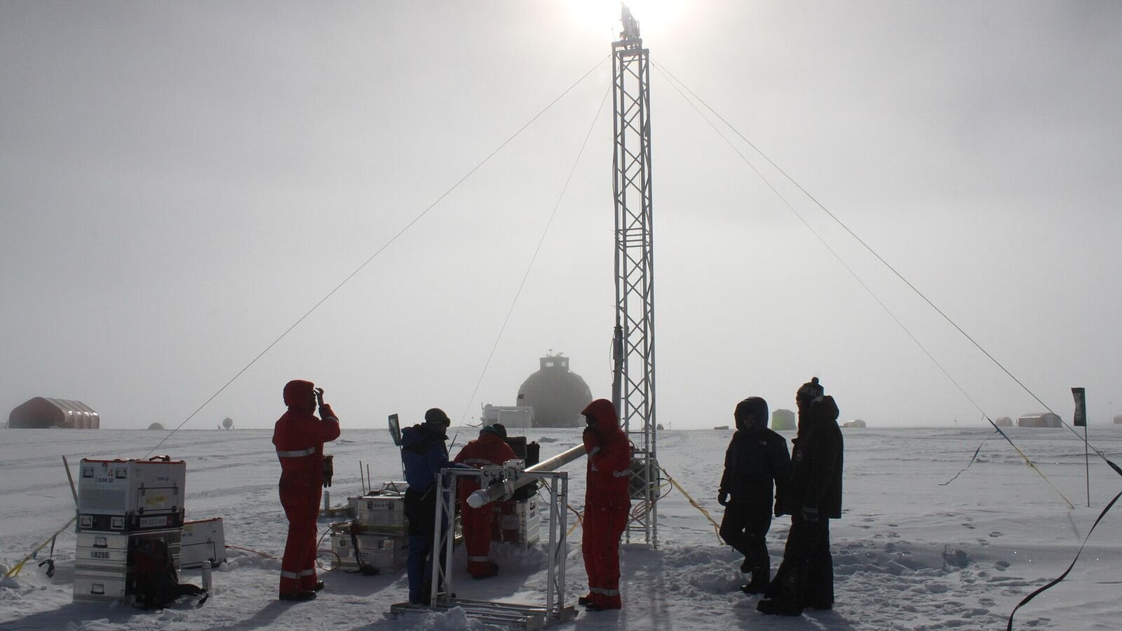 Researchers in cold-weather clothing working with a drilling rig on the snow surface at an ice core camp in Greenland.