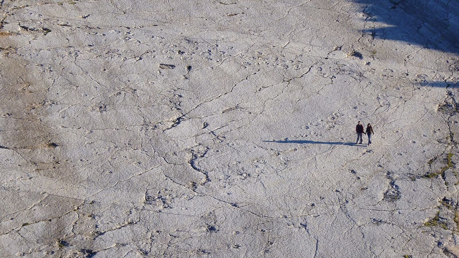 A vast pale limestone slope covered in rows of large round depressions, with two people standing on it for scale, dwarfed by the size of the surface.
