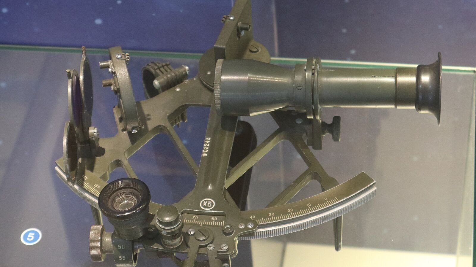 A brass and metal navigation sextant on display, showing its graduated arc, index arm, mirrors and small telescope.