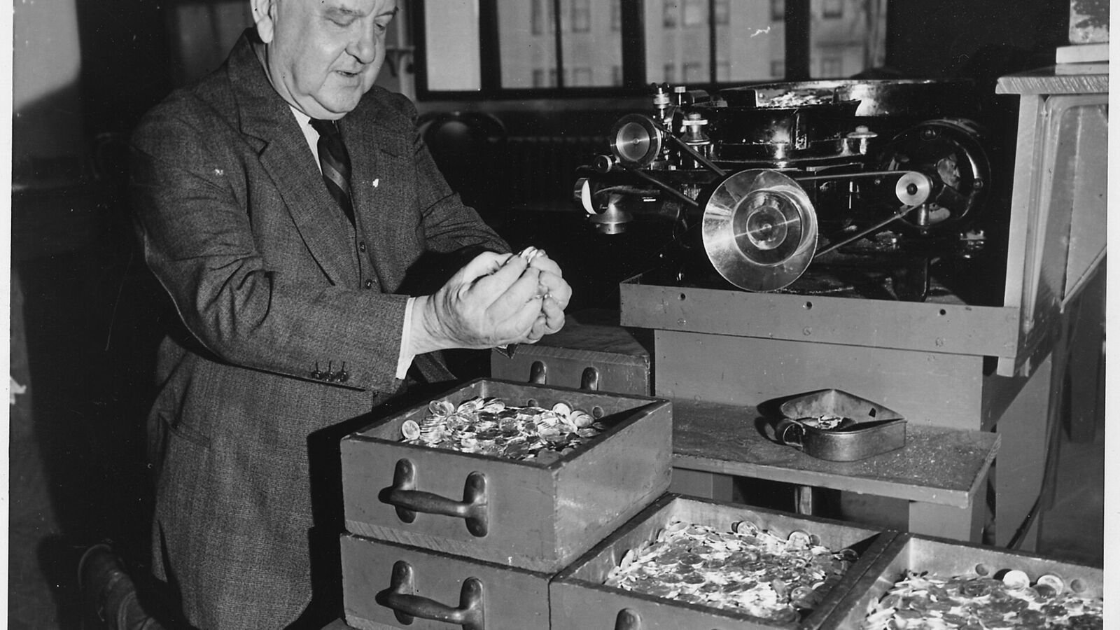 Workers in shirtsleeves operating coining presses on the floor of the San Francisco Mint, with trays and sacks of blank coins beside the machines.