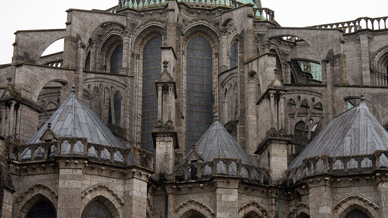 The east end of Chartres Cathedral seen from outside, showing tall stone window bays, pinnacled piers and half-arches of masonry springing across to meet the upper walls.